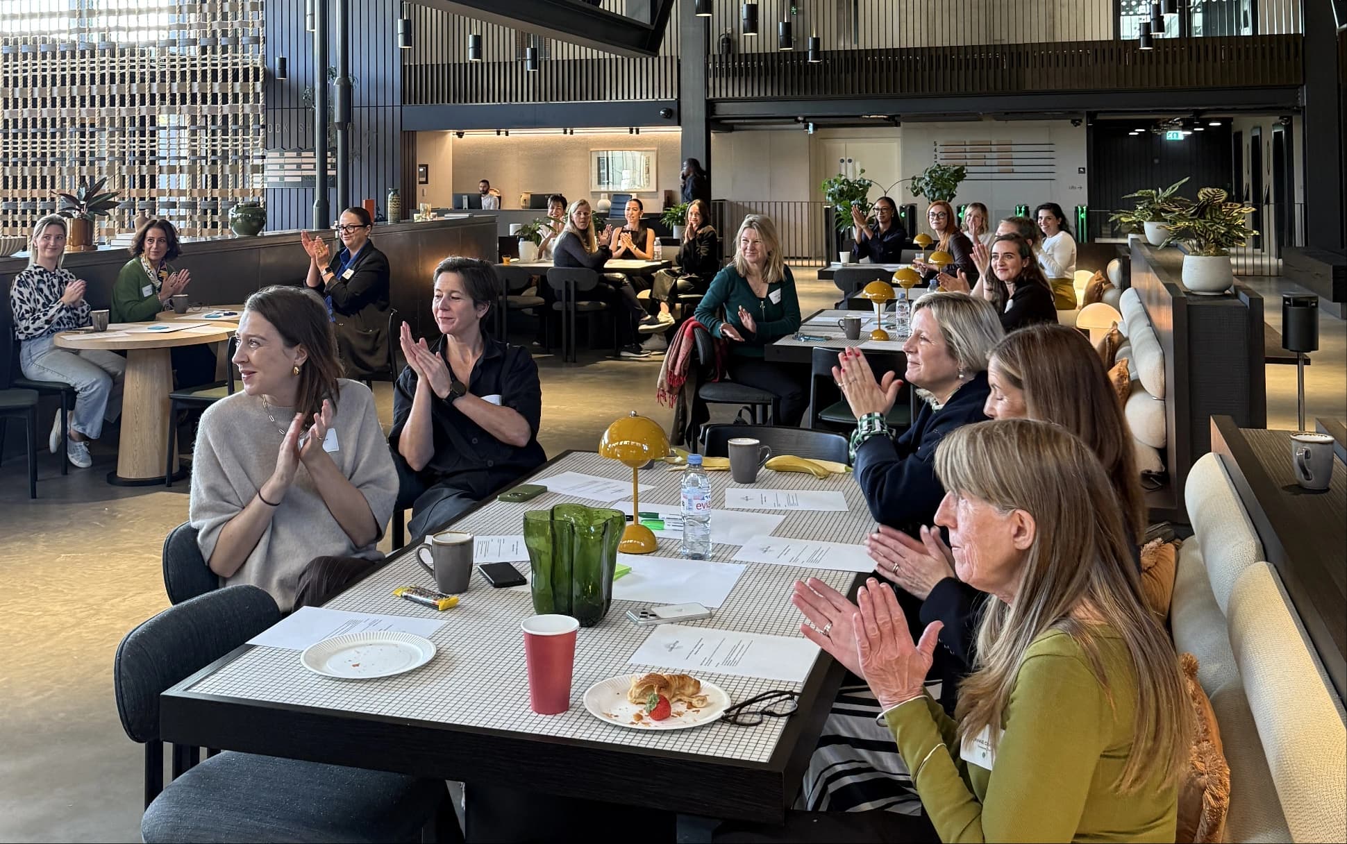 Rooftop terrace at sunset with outdoor dining table and lounge seating overlooking the London skyline, sunlight flaring beside a modern building facade.